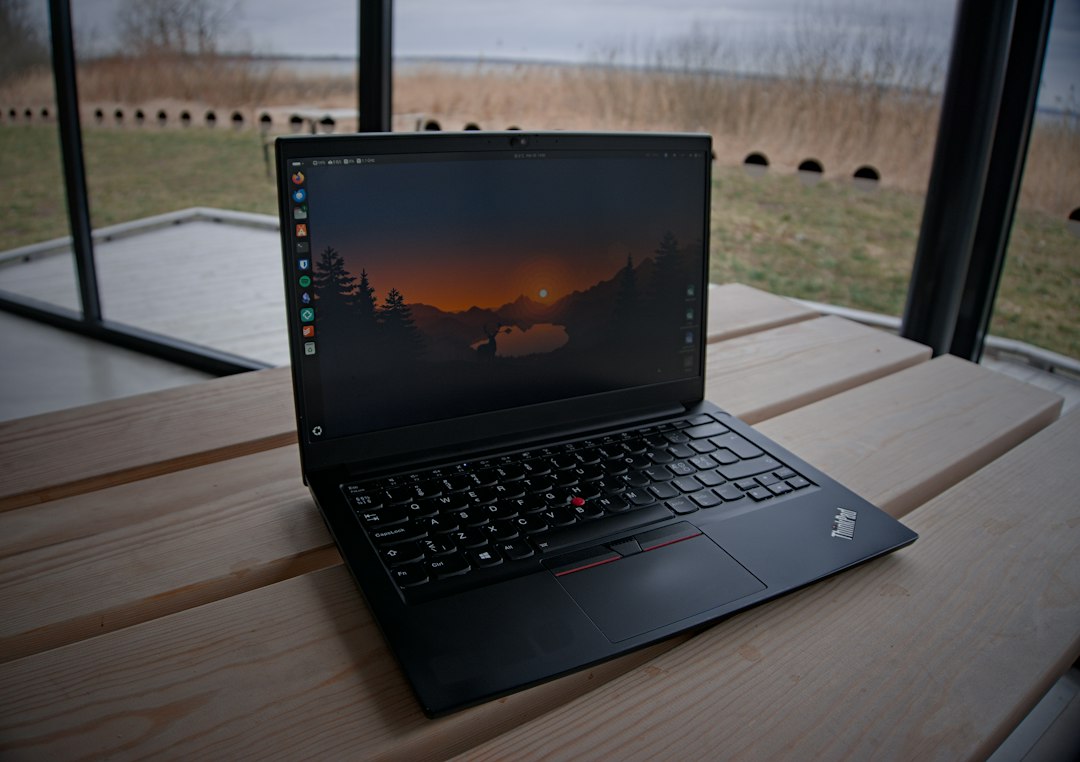 Lenovo ThinkPad T14s Gen 1 i7 : fiabilité en 2026 ? 1 Lenovo ThinkPad laptop ouvert sur une surface en bois avec vue sur un lac en arrière-plan